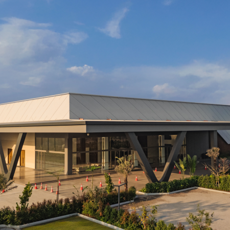 Daytime exterior view of the Neo Convention Center, showcasing its modern architecture with large glass windows and sleek design, set against a bright blue sky and sunny weather.
